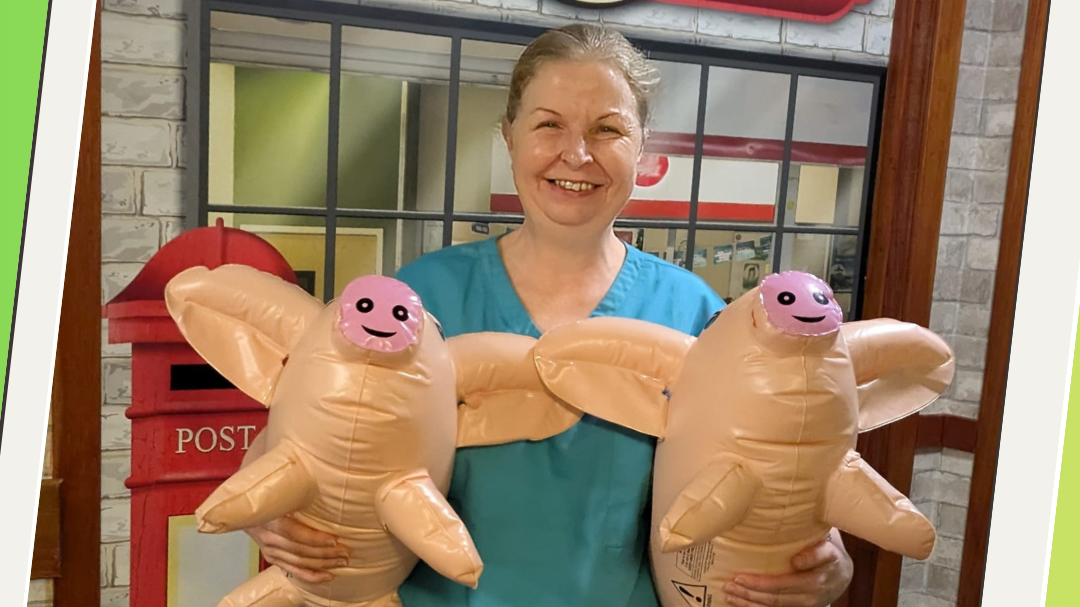 Activity Co-ordinator stood holding inflatable pigs and smiling