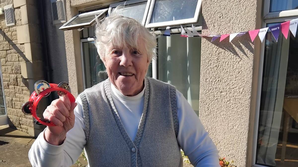 Resident of willow house pictured outside the home shaking a tambourine smiling